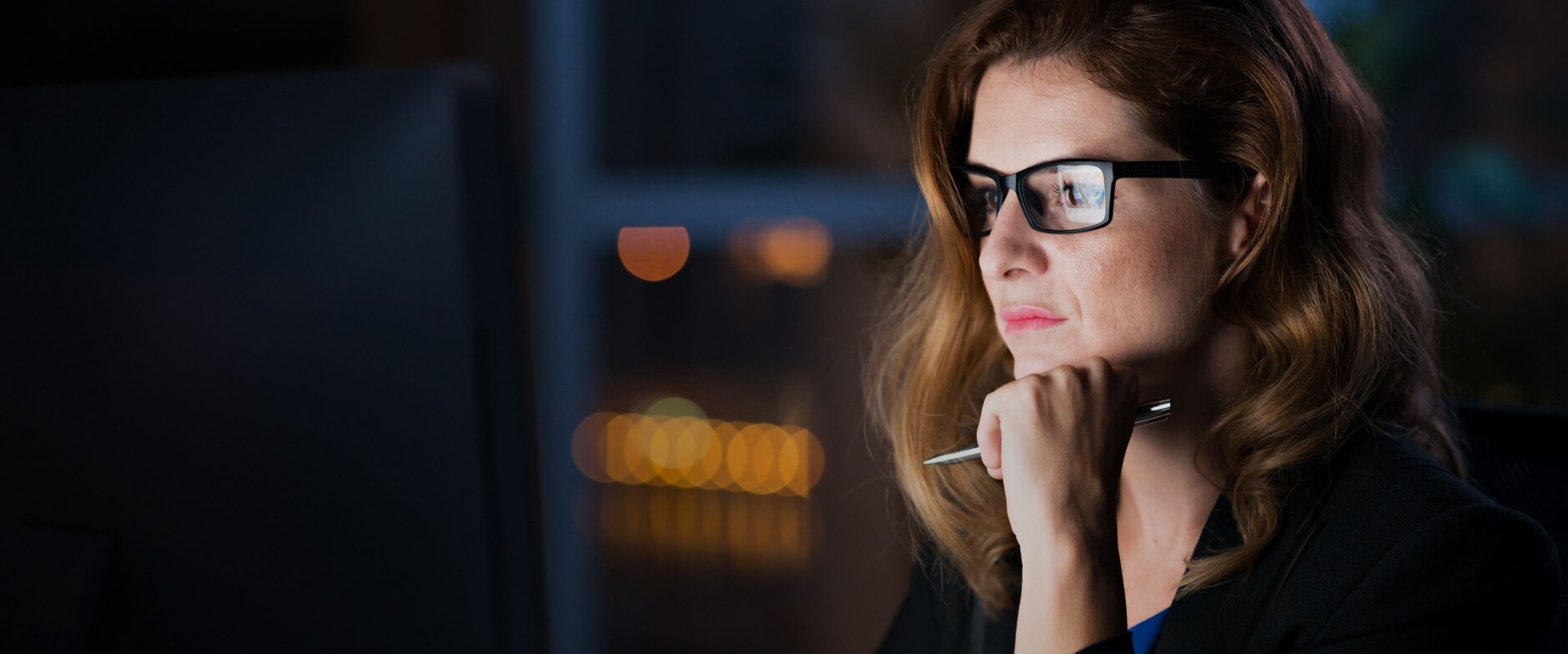 Person, die eine Brille trägt, auf einen Computer schaut und einen Stift in der Hand hält