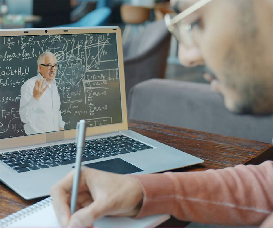 Person, die auf einen Laptop-Computer mit angezeigter Tafel blickt und sich dabei Notizen macht