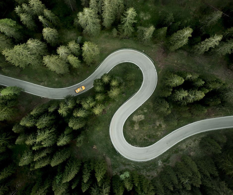 Vista aerea di un'auto che percorre una strada tortuosa attraverso la foresta.