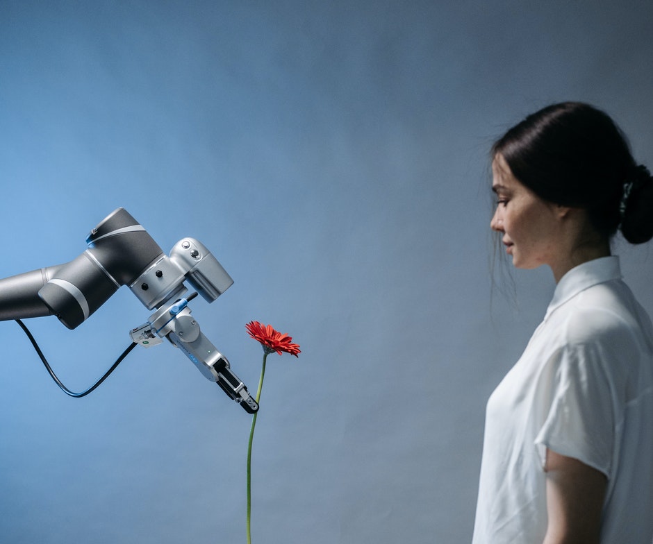 A machine holding a rose and a person looking at it