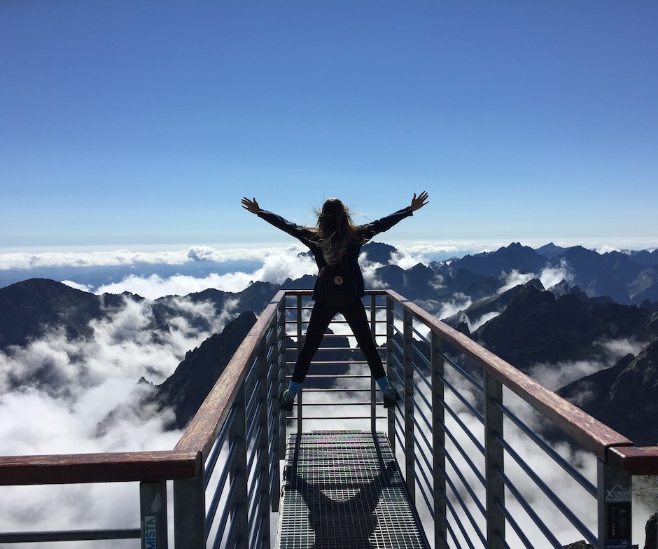 person standing on railing cliff looking at snow mountains