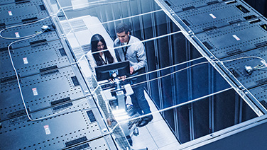 Two people between two racks of storage systems looking at a screen